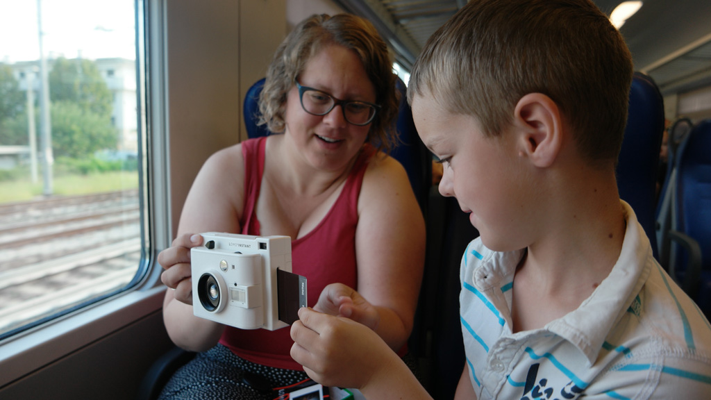 De camera in de trein uitproberen. Verbaasde blik bij de kinderen als er zomaar een foto uit de camera rolt.
